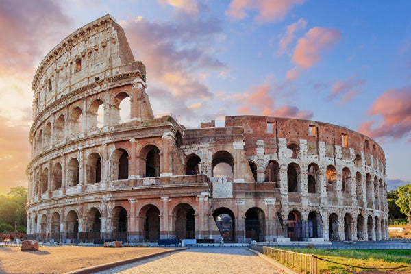 Exterior of the Colosseum in Rome lit up by the golden afternoon blue sky with clouds tinged pink and purple