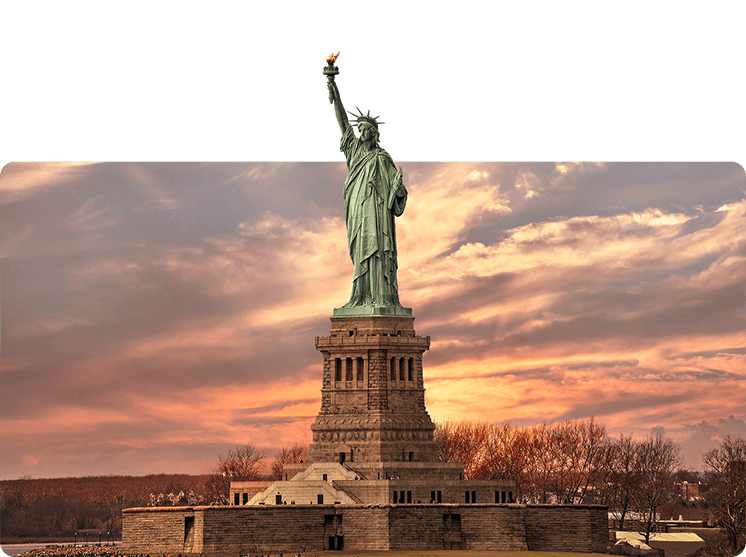 The Statue of Liberty in New York in front of a hazy sunset sky filled with orange and pink clouds 