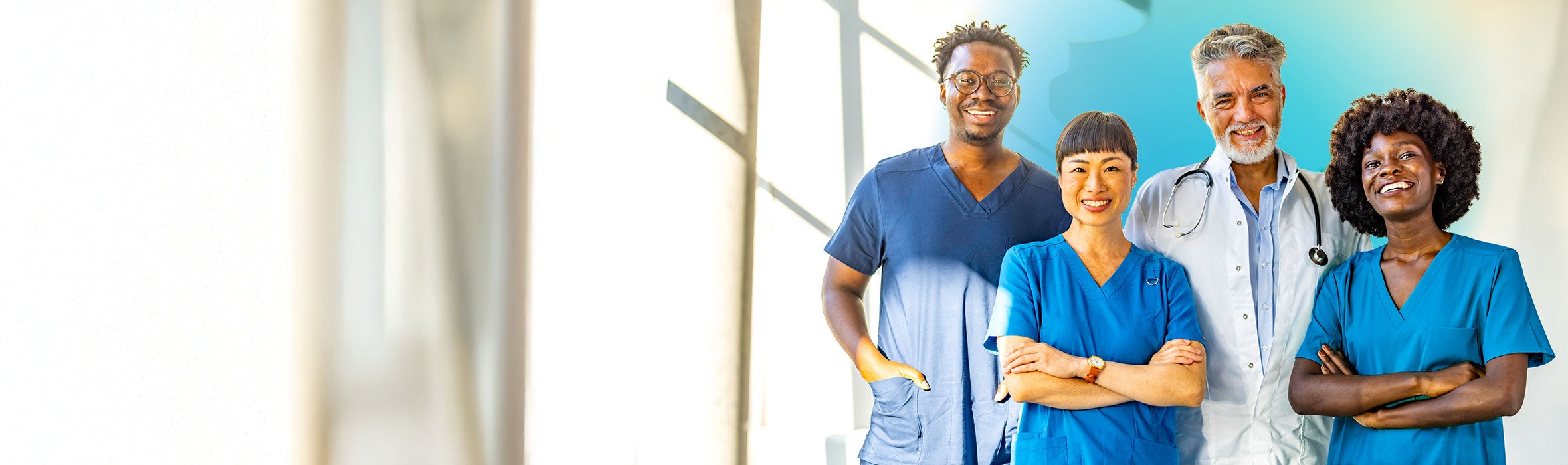 A group of four multiracial medical professionals smiling and wearing blue scrubs with blurred background and blue gradient hovering over them 