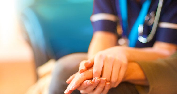 Closeup of a medical professional's hands holding hands with a patient to comfort them 