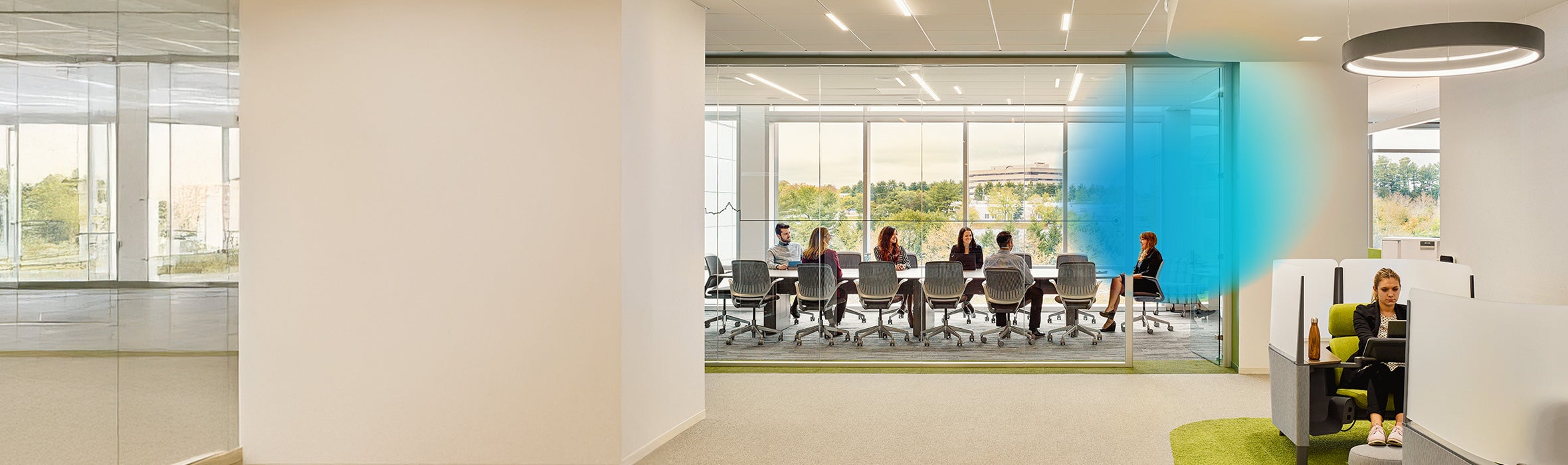  A group of working professionals in a conference room with a blue gradient around the woman at the head of the table and an overlaying closer up image of a woman working independently at her desk
