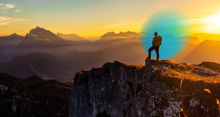 Man wearing a backpack on the top of a mountain surrounded by other mountains during the sunset and a blue gradient hovering around him 