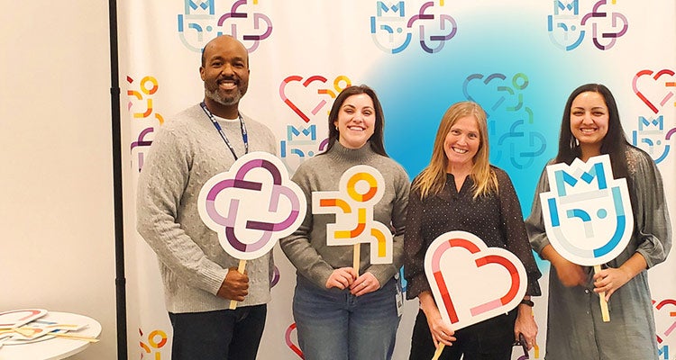 A group of four multiethnic employees at work holding colorful signs representing core values with a blue gradient hovering around them 