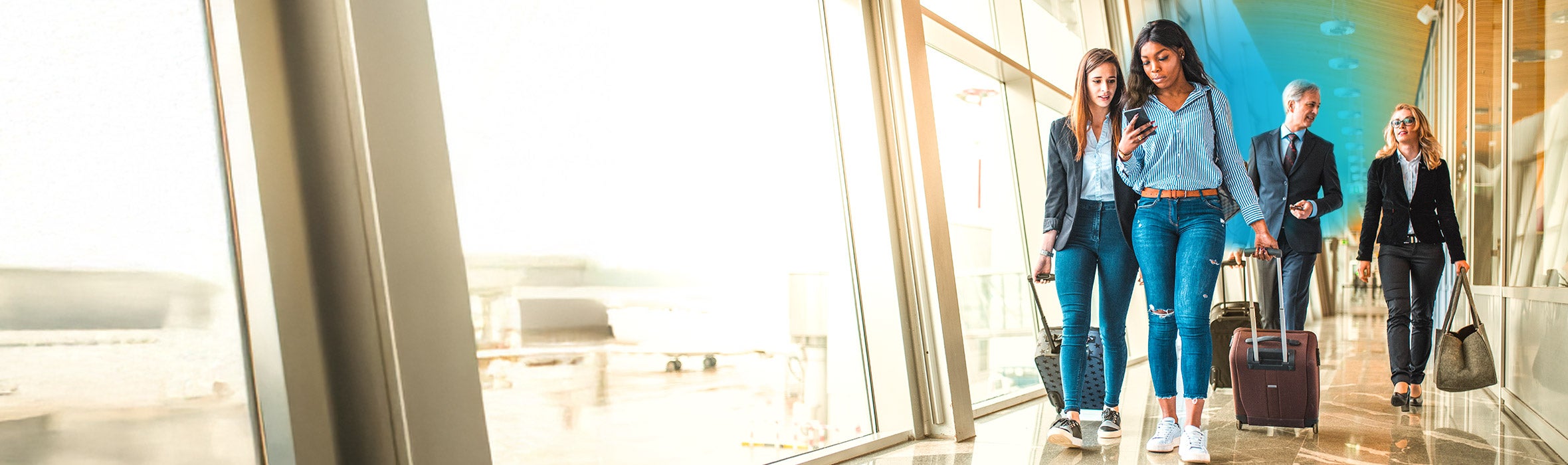 Two female friends and a businessman and woman walking behind them all rolling suitcases in an airport by a big window and blue gradient hovering around them 