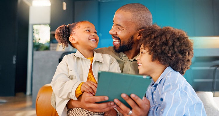 Smiling African American father sitting with his two young smiling children at home while he's holding a tablet 