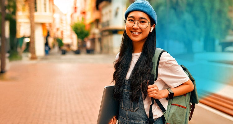 Smiling Asian woman outside wearing glasses and holding a laptop and backpack with blue gradient hovering around her 