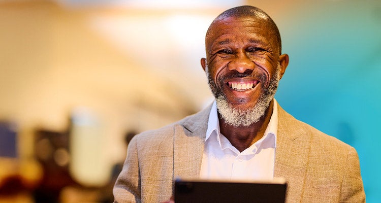 Older African American man smiling and holding a tablet with a blurred background and blue gradient hovering around him  