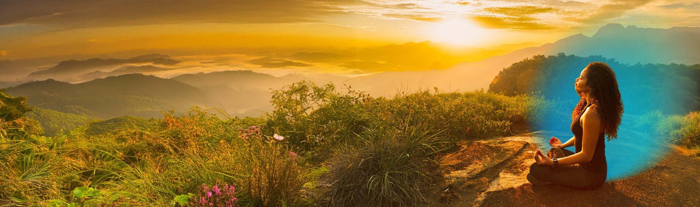 Young African American woman with curly hair wearing yoga outfit meditating on a mountain filled with plants and flowers as the sun sets in the distance
