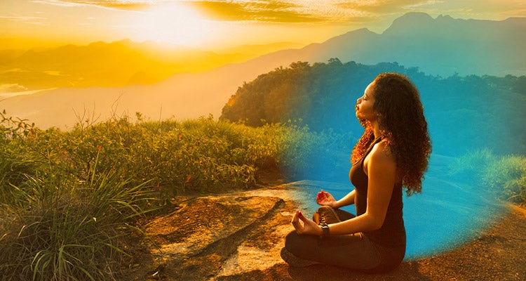 Young African American woman with curly hair wearing yoga outfit meditating on a mountain filled with plants and flowers as the sun sets in the distance