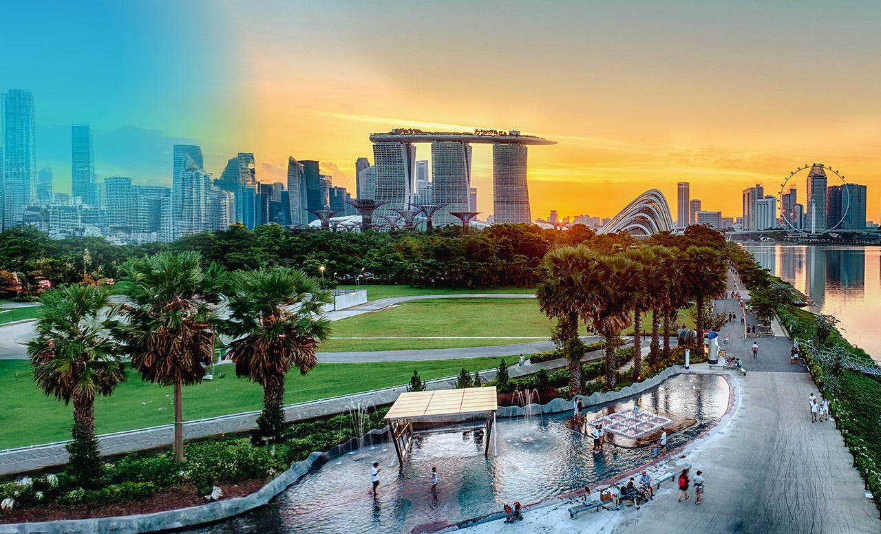 A modern city skyline with skyscrapers and green spaces with palm trees and water in the foreground 