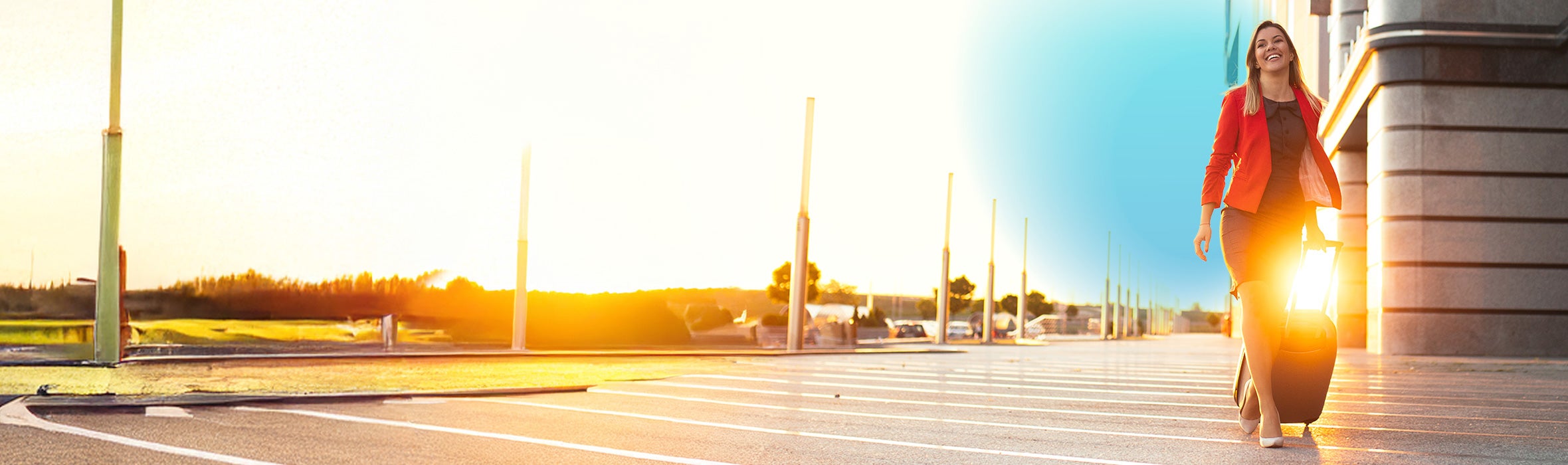 Businesswoman wearing a red blazer and black dress smiling while rolling a suitcase in a parking lot during the sunset with blue gradient hovering over her 
