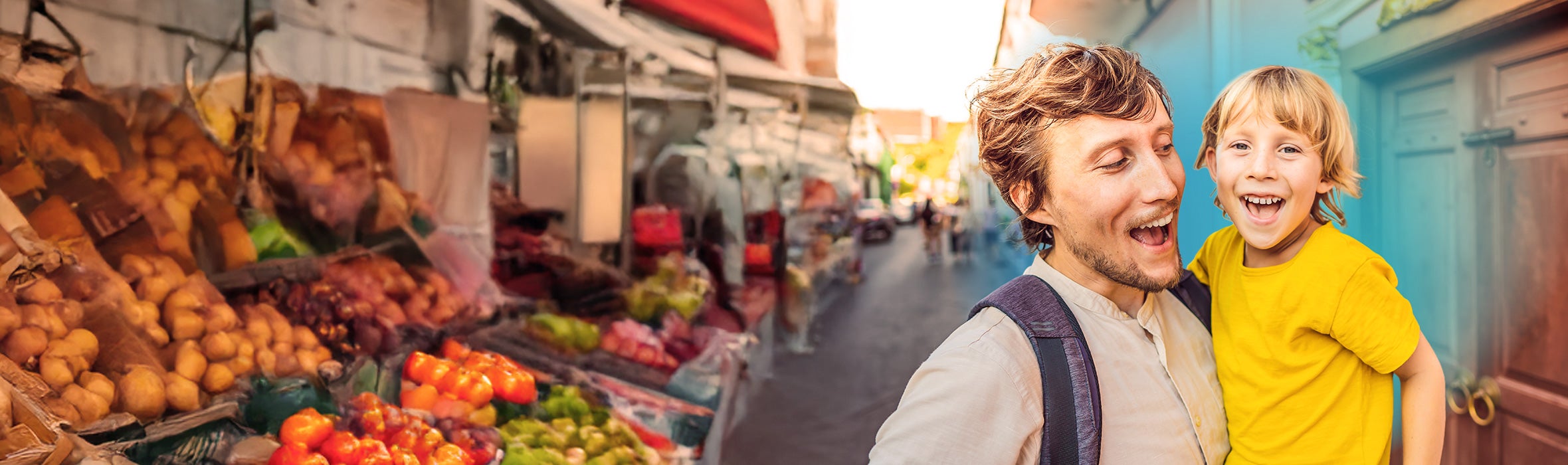Caucasian man holding young son both smiling and walking pass a fruit and vegetable market outside 
