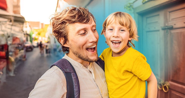 Caucasian man holding young son both smiling and walking pass a fruit and vegetable market outside
