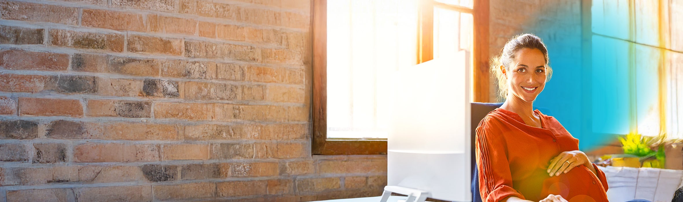 Smiling pregnant businesswoman sitting at computer desk with blue circled gradient hovering around her