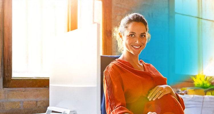 Smiling pregnant businesswoman sitting at computer desk with blue circled gradient hovering around her