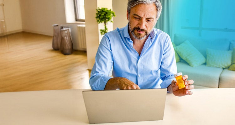 Middle aged man sitting down holding a pill bottle while typing on his laptop and blue gradient hovering to the right of him