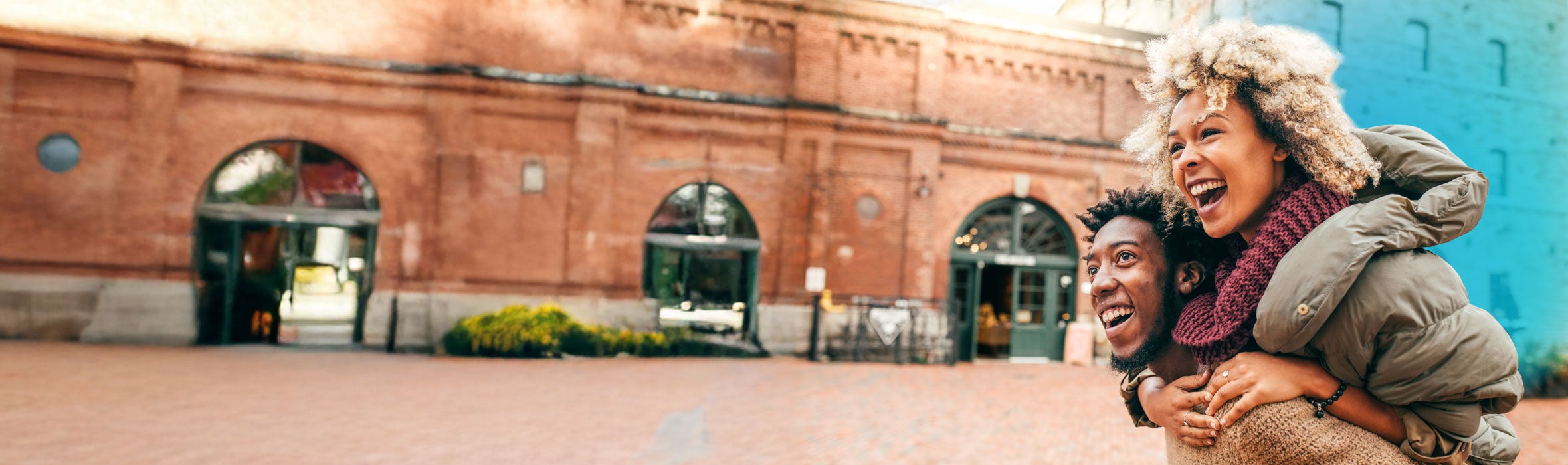 A young African American couple wearing sweaters and coats smiling walking in front of a historic building 