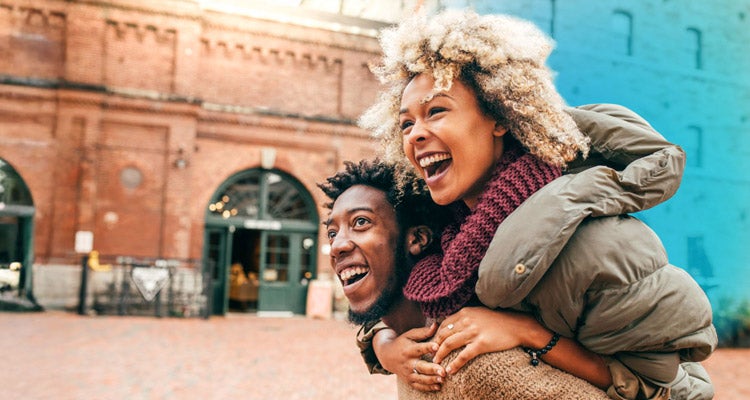 A young African American couple wearing sweaters and coats smiling walking in front of a historic building 