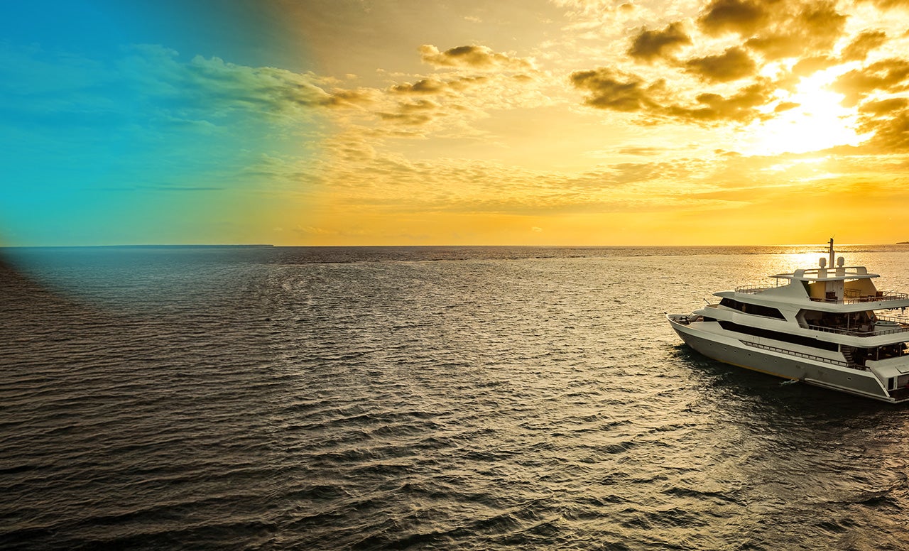 Open sea lit up by late afternoon sunshine with a white yacht gliding on the water 