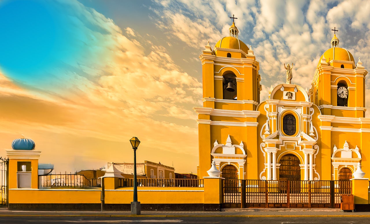 Intricate Spanish-style orange and white Cathedral in front of a sky filled with orange-tinted clouds 