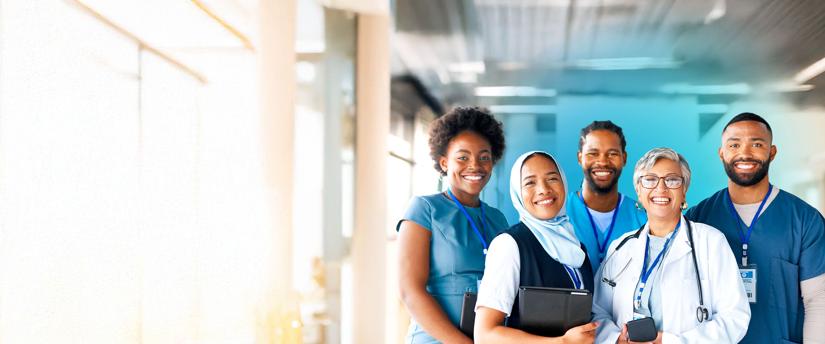 A group of multiethnic medical professionals wearing shades of blue smiling inside a hospital 