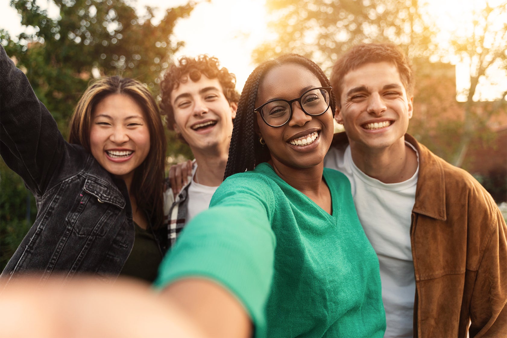 Group of four racially diverse young adults smiling in front of trees on a sunny day on campus 