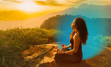 Woman wearing black sitting in a mountain area during the sunset while meditating with blue circle hovering around her 