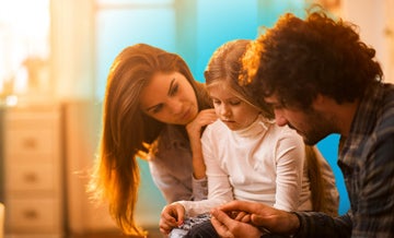 Sad little girl sitting between two parents being consoled by them and blue circled gradient hovering behind them
