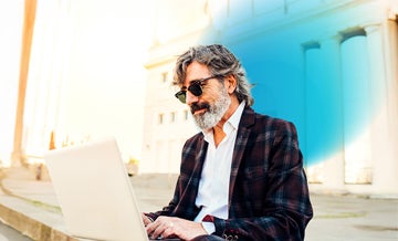 Older businessman sitting outside working on his laptop and blue circled gradient hovering around him
