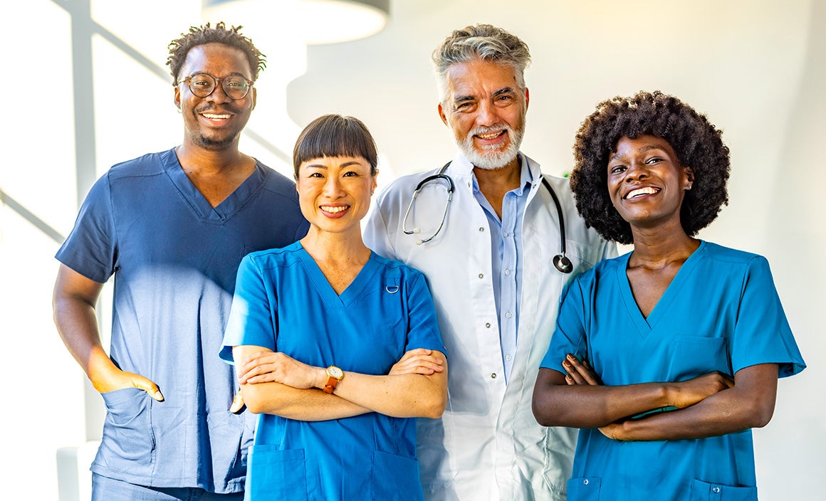 A group of four multiracial medical professionals smiling and wearing blue scrubs with blurred background