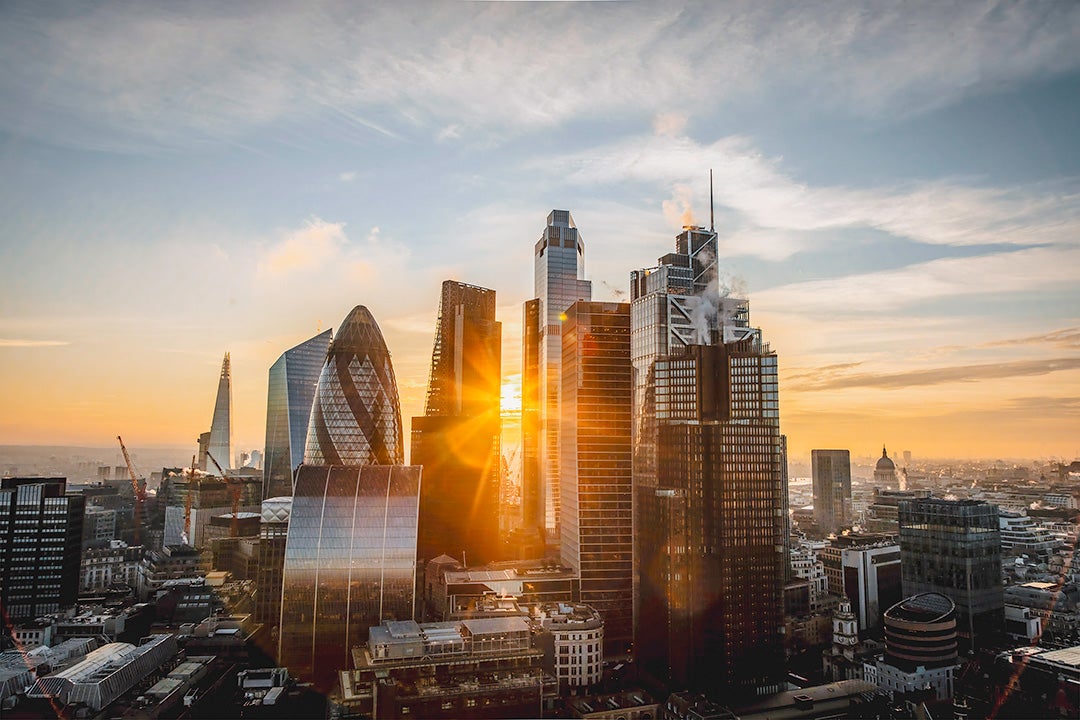A city skyline with tall Highrise buildings in the center with the sunset beaming behind the buildings 