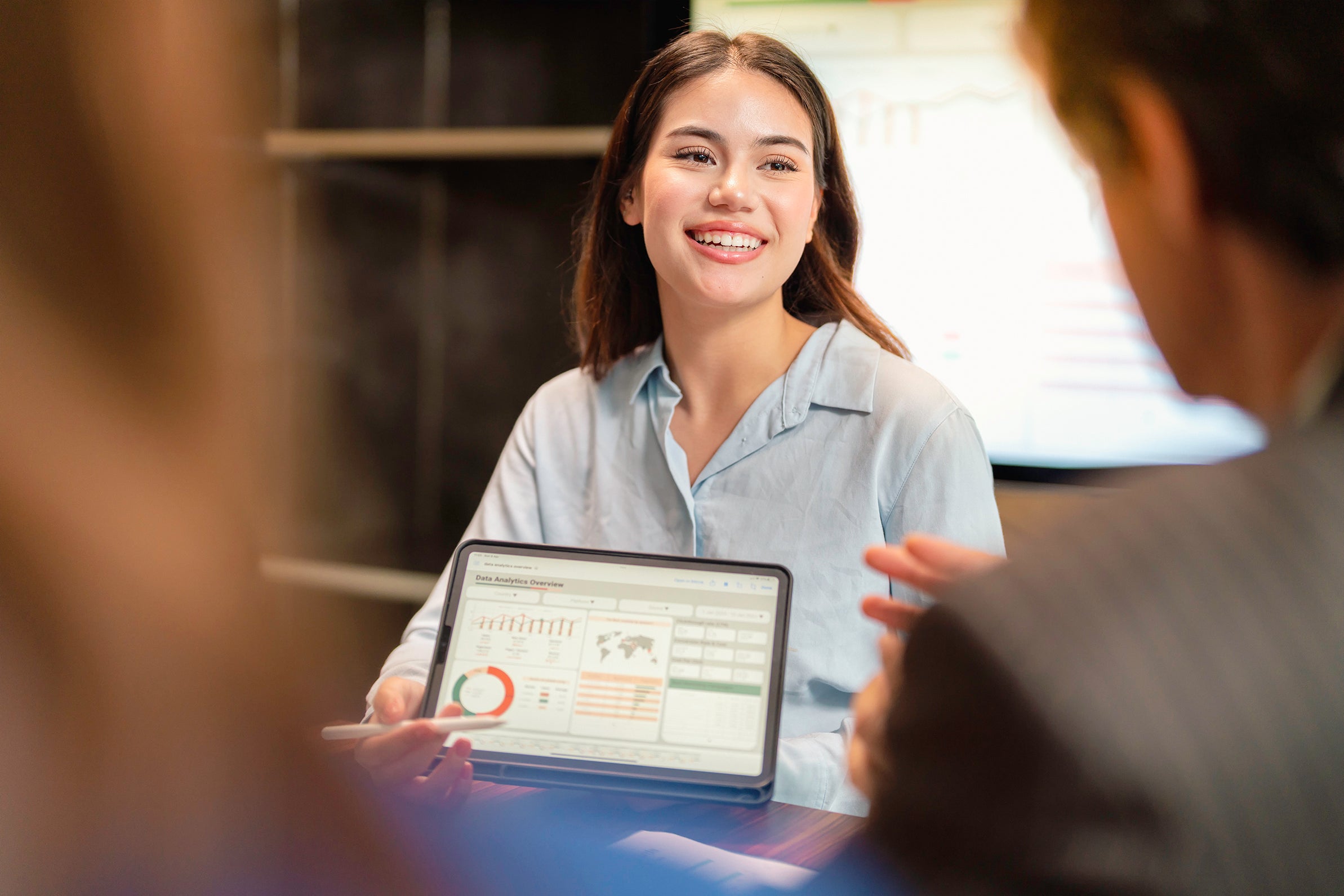 Woman smiling in a business meeting showing analytics presentation overview on her tablet 