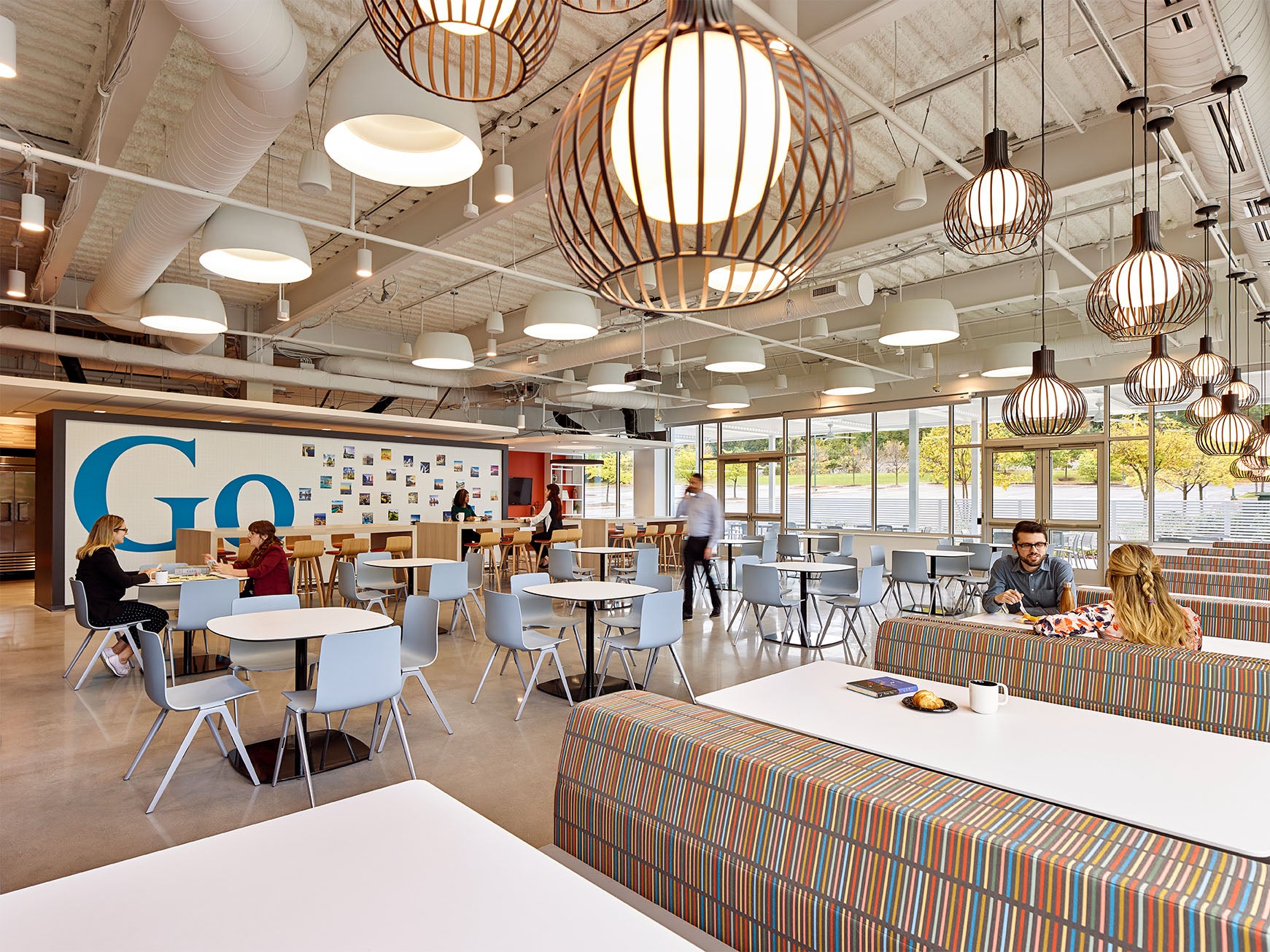 Modern corporate cafeteria with booth seating and tables and chairs with coworkers sitting, talking and eating 