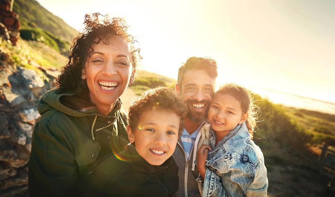 Young African American woman in a green jacket and her Caucasian husband in a blue grey jacket and their two children smiling for a picture on vacation in the golden sunlight 
