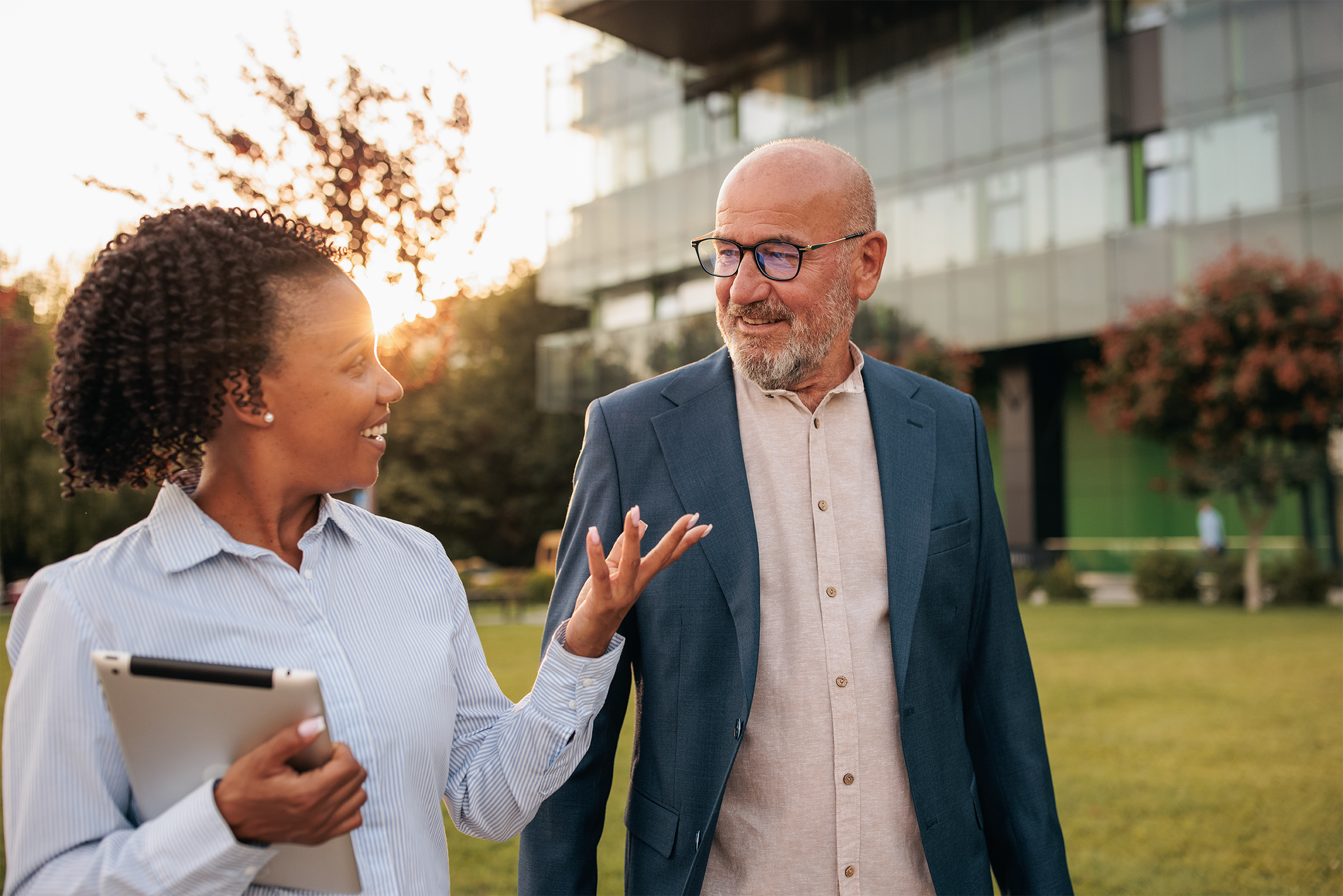 A businesswoman and businessman walking outside talking and smiling with each other 