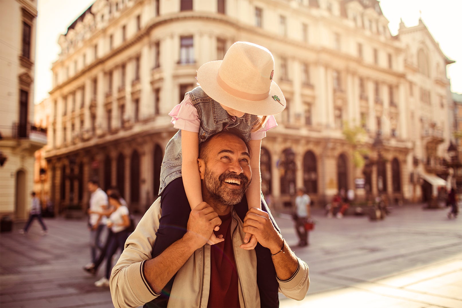 Middle aged Caucasian father holding his daughter on his shoulders while walking through a charming European city 